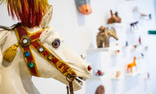 Head of a white roundabout-horse with colourful harness and in the background a white wall with toys in form of animals